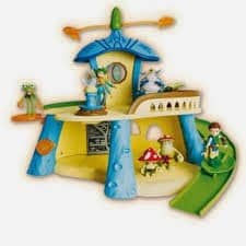 Colourful toy playset resembling a whimsical house with blue columns, yellow walls, green slide, and cartoon character figurines, including fairies and animals, placed around the structure, evoking a magical, storybook atmosphere.