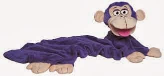 A soft toy shaped like a smiling purple monkey with beige face, ears, hands, and feet. The monkey’s body is long, flat, and blanket-like, and its large eyes and open mouth give it a playful appearance.