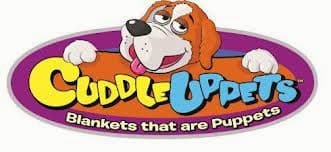 A cartoon dog with brown and white fur leans over an oval purple sign. The yellow and blue text reads “Cuddle Uppets.” Below, in white letters, it says, “Blankets that are Puppets.”.