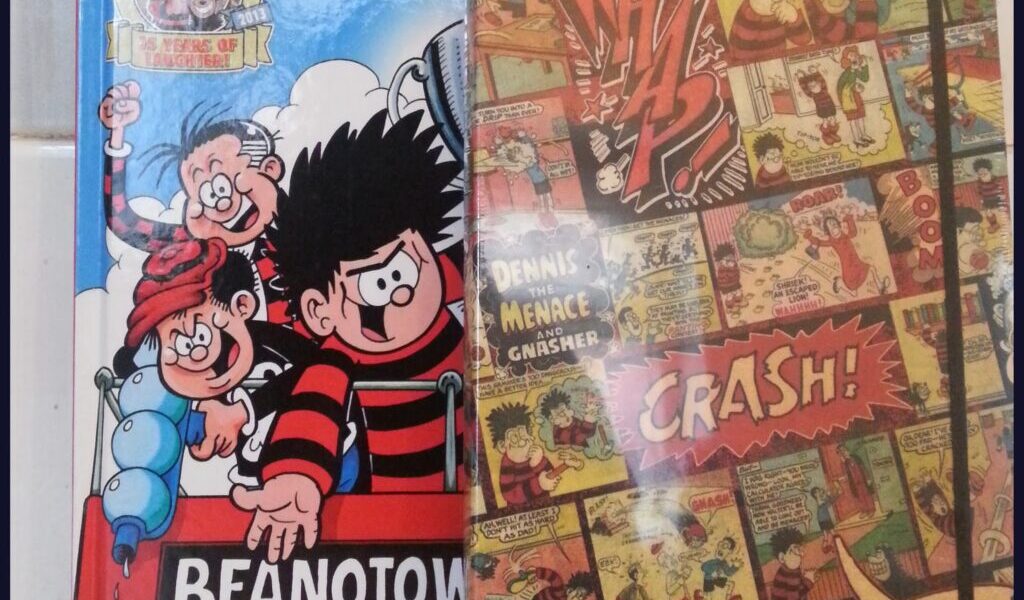 Two comic books are shown. The left one is the "Beano Annual 2014" featuring cartoon characters, including Dennis the Menace, smiling on the cover. The right book has a collage of vintage comic panels with bright sound effects like “CRASH!” and “ARGH!”.
