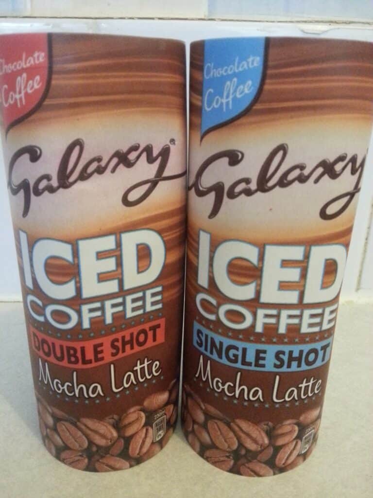 Two cylindrical containers of Galaxy Iced Coffee Mocha Latte stand side by side. The left is labelled "Double Shot," the right "Single Shot." Both feature an image of coffee beans and a swirl of chocolate, with blue and red accents on the text.