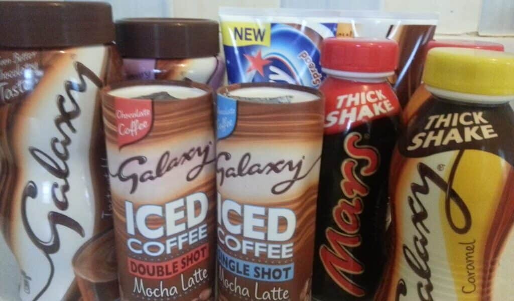 Assorted chocolate drinks on a counter, including Galaxy Iced Coffee (Mocha Latte Double Shot, Mocha Latte Single Shot), Galaxy Thick Shake Caramel, Galaxy drinking chocolate, Mars Thick Shake, and a partially visible Milky Way product in the back.