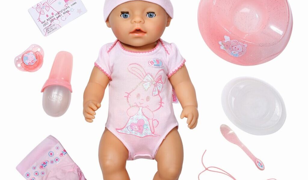 A baby doll wearing a pink hat and bunny onesie is surrounded by toy accessories: a nappy, bottle, dummy, bowl, plate, spoon, bracelet, necklace, bottle top, and illustrated cards, all in shades of pink and white on a white background.