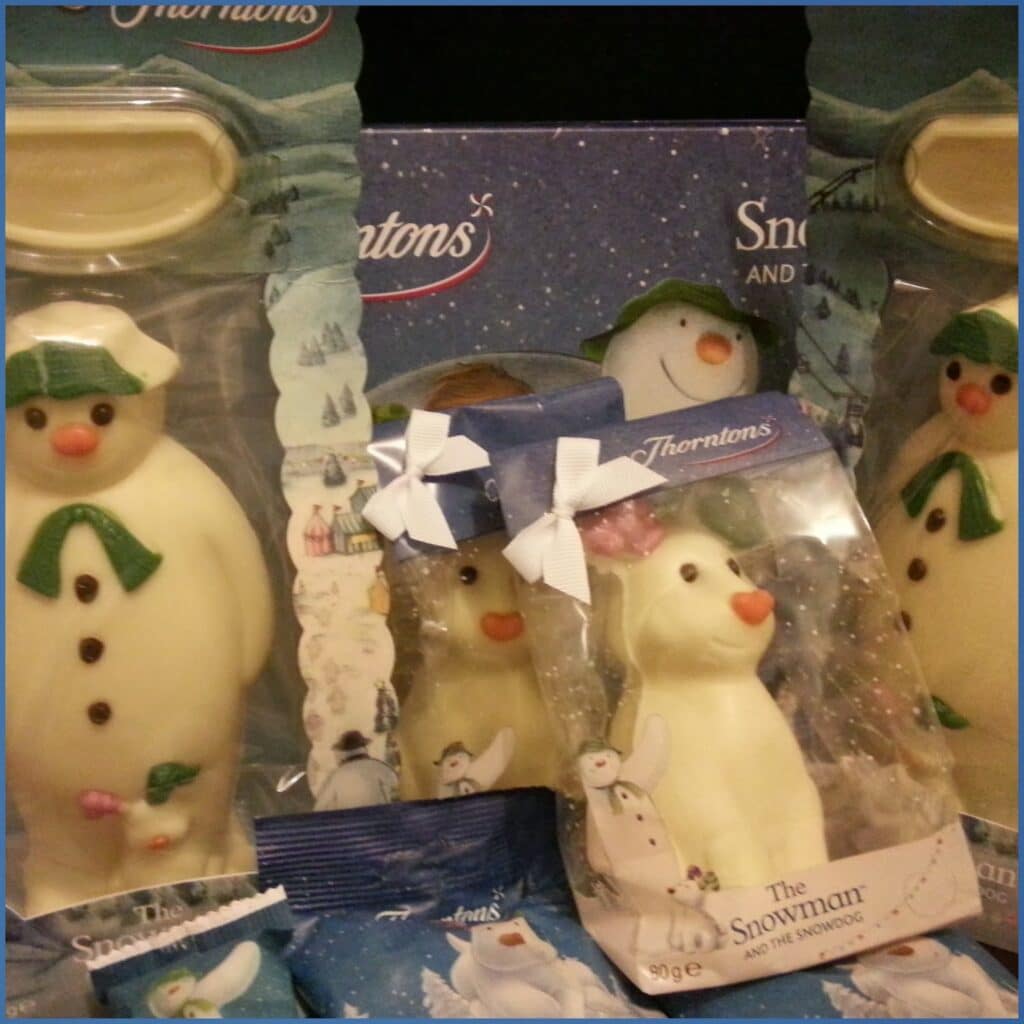 Assorted white chocolate snowman figures in festive packaging labelled “Thorntons”, with various sizes and boxes. All snowmen wear green hats and scarves, and some have bows. Background and wrappers feature snowy winter scenes.