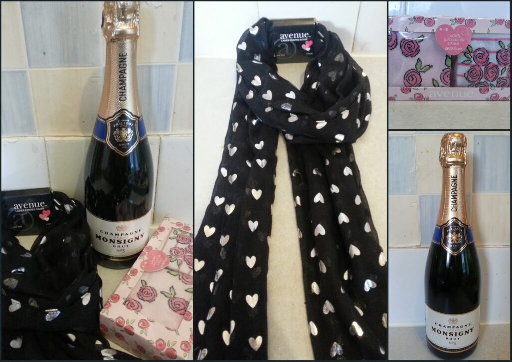 A collage shows a bottle of Monsigny champagne, a black scarf with white hearts, a box with a pink rose pattern, and a bar of Avenue chocolate. Images display these gift items together and individually against a light, tiled background.