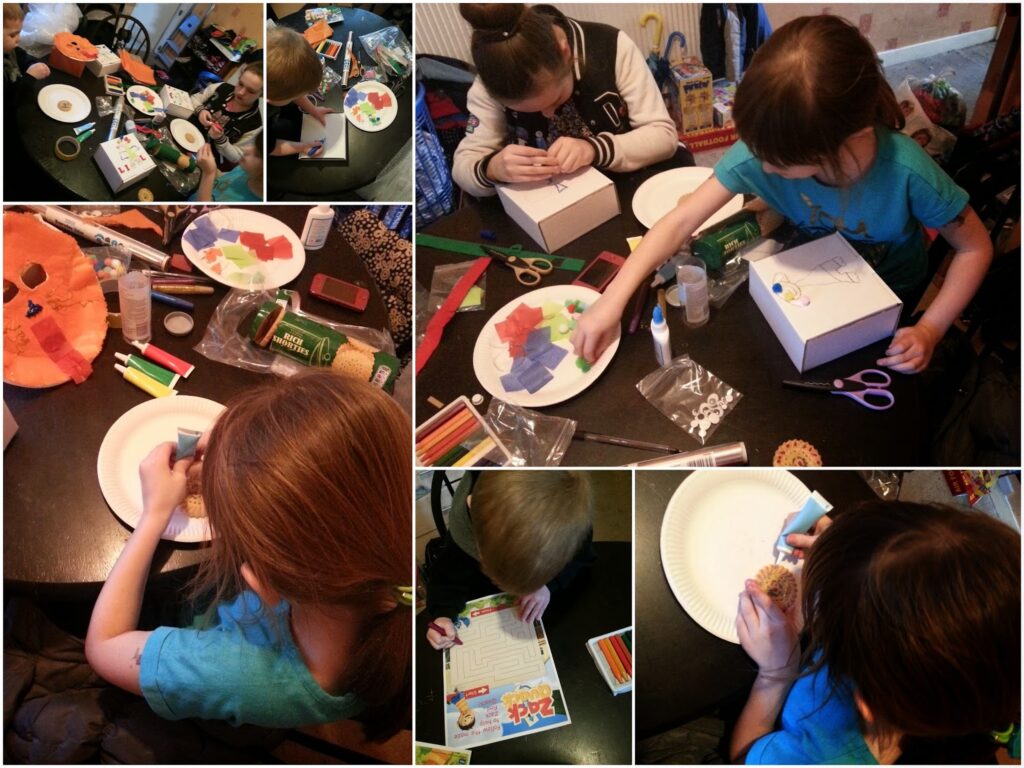 A collage of children at a table doing various arts and crafts: sticking coloured paper, drawing on boxes, and working with craft supplies like scissors, felt-tip pens, pom-poms, googly eyes, and plates, all set on a dark tabletop in a cosy room.