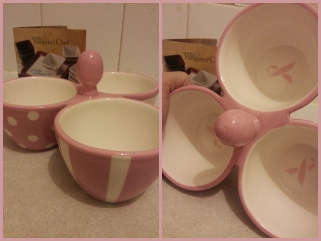 A ceramic bowl set with three pink and white bowls attached at the base. One bowl has polka dots, another has stripes, and the third is solid pink. The underside of each bowl features a pink awareness ribbon. Pampered Chef boxes are in the background.