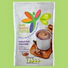 A packet of "Good Healthy Living" instant hot chocolate is shown. The packaging displays a cup of hot chocolate on a wooden tray with biscuits. It mentions "39 calories" and "just add hot water." The background is light green.
