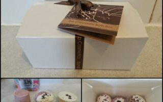 A rectangular white box with a brown ribbon and tag reading “The Chocolate Bath Box.” Below, bath bombs in pink, white, and brown shades, some with decorative toppings, are arranged on a surface and inside an open box.