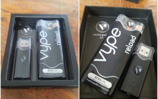 A black box contains a Vype Reload rechargeable e-cigarette kit. Inside are a USB charger and a rectangular black e-cigarette device labelled “vype reload.” Both items have matching branding. The box and its contents rest on a wooden surface.