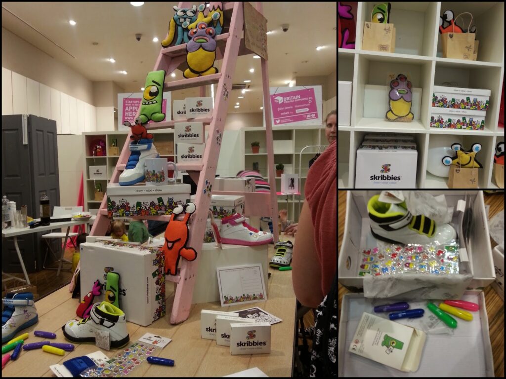 A craft display shows custom-decorated trainers on a pink ladder surrounded by colourful cartoon plush toys, markers, sticker sheets, and Skribbies boxes. Nearby shelves hold more plush characters and crafted shoes in a bright, modern shop setting.