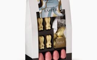 A gift box containing white chocolate bunny shapes, a gold-foiled bunny, and five pink foil-wrapped eggs. The packaging has a decorative label reading “Pick Me Up Easter” with pastel colours and a clear window showing the chocolates inside.