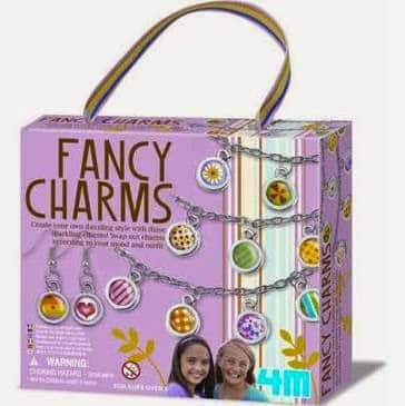 A purple “Fancy Charms” craft kit box with colourful charm designs shown on necklaces. The box features photos of two smiling girls and a warning label. A striped handle is attached at the top. The brand “4M” appears in the bottom right corner.