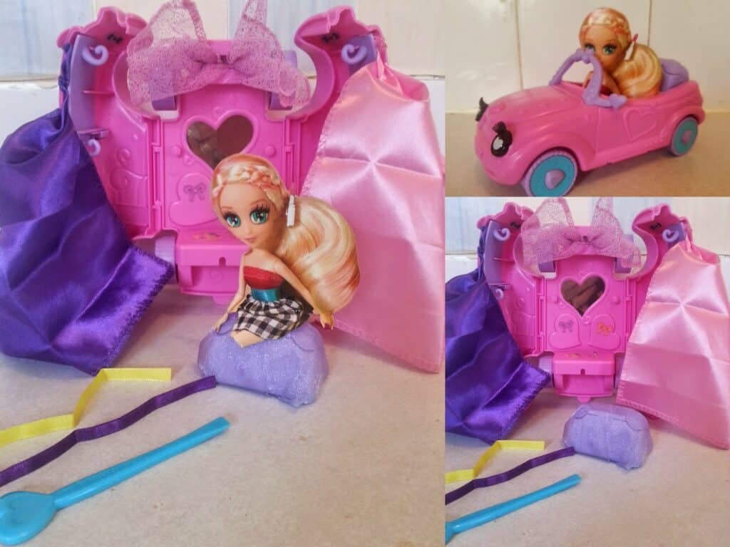A blonde doll in a checked skirt sits on a glittery purple rock in front of a pink, heart-shaped case with purple and pink fabric curtains. Nearby are a blue spoon, yellow ribbon, and a pink toy car with the same doll seated inside (shown in inset).