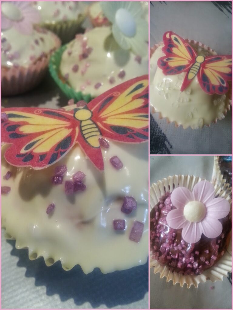A collage of cupcakes topped with white icing. One cupcake features an edible red and yellow butterfly, another has a pink flower, and a third includes a pale flower with a green wrapper. All are sprinkled with purple sugar crystals.