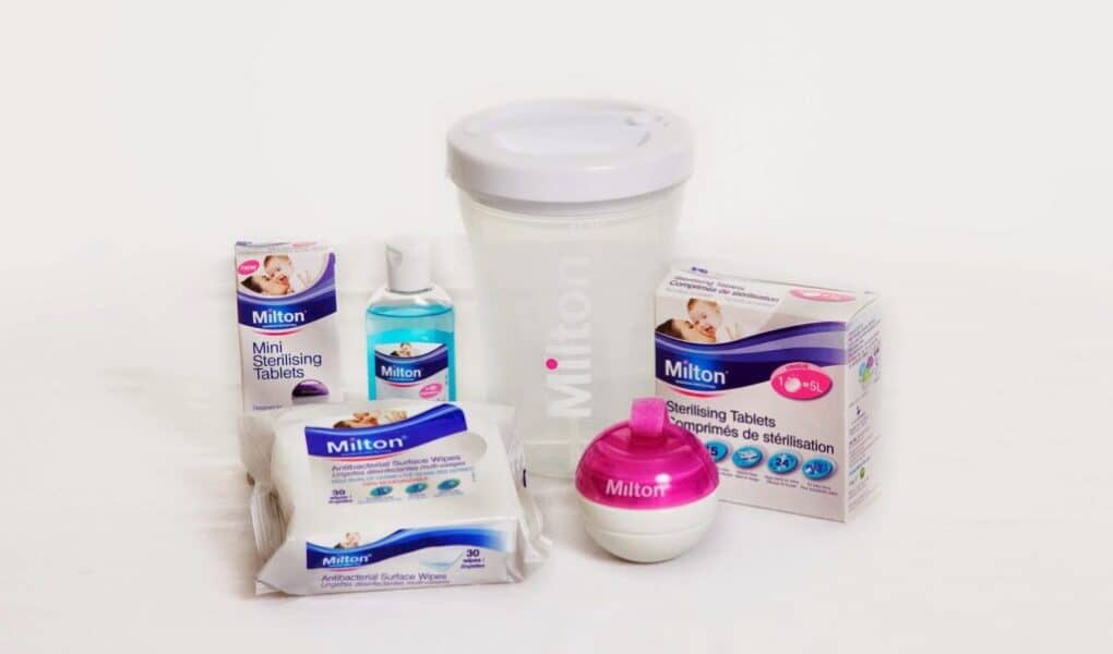 A collection of Milton baby sterilising products, including mini sterilising tablets, sterilising fluid, surface wipes, sterilising tablets, a large white sterilising container with lid, and a pink-and-white soother steriliser, all displayed on a white background.