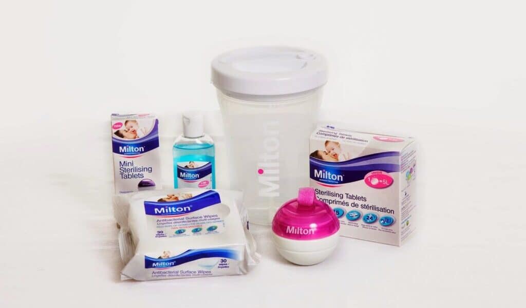 A collection of Milton baby sterilising products, including mini sterilising tablets, sterilising fluid, surface wipes, sterilising tablets, a large white sterilising container with lid, and a pink-and-white soother steriliser, all displayed on a white background.