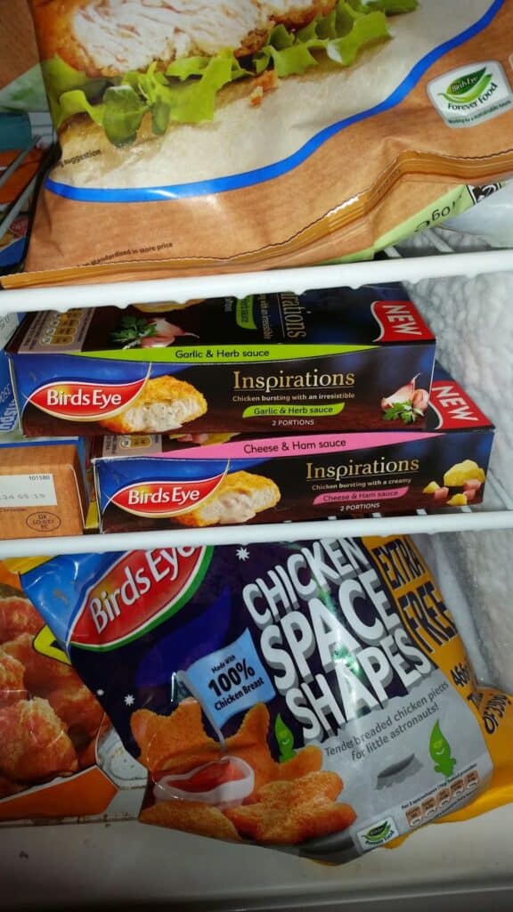 Frozen food items in a freezer, including Birds Eye Inspirations meals in Garlic & Herb and Cheese & Ham sauces, and a bag of Birds Eye Chicken Space Shapes. The freezer has a white wire shelf and a frosty white background.