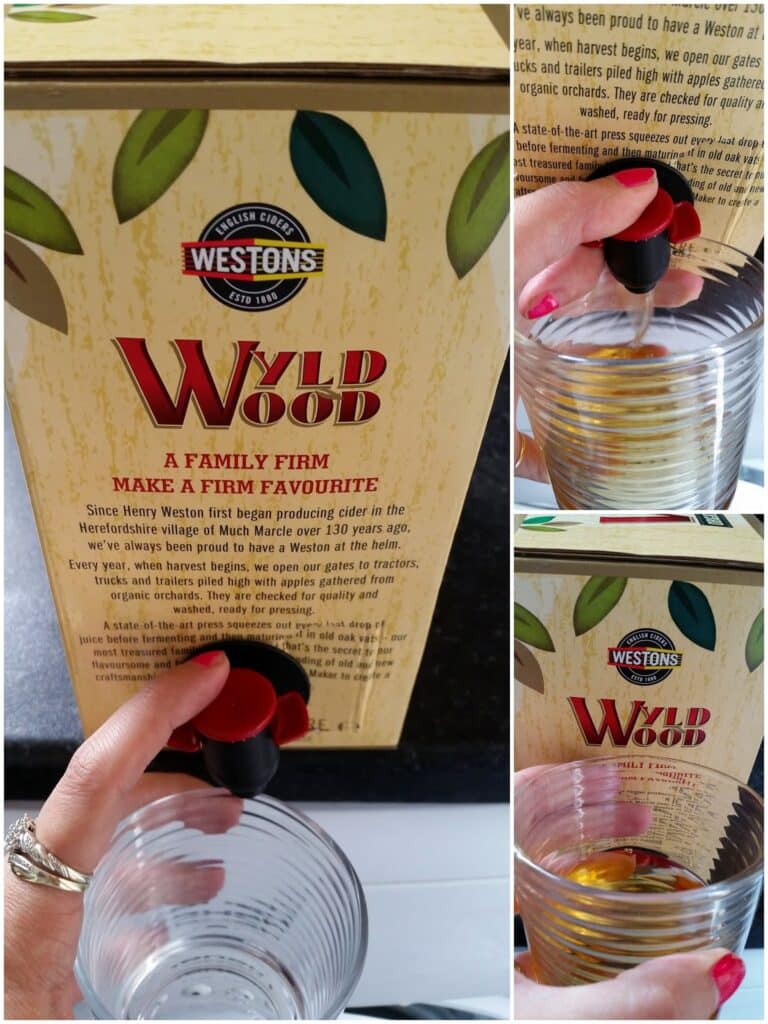 A hand holds a glass under the tap of a large box of Westons Wild Wood English Cider, dispensing the drink. The box has a rustic design with leaves, bold red "Wild Wood" text, and descriptive info about the cider's heritage.