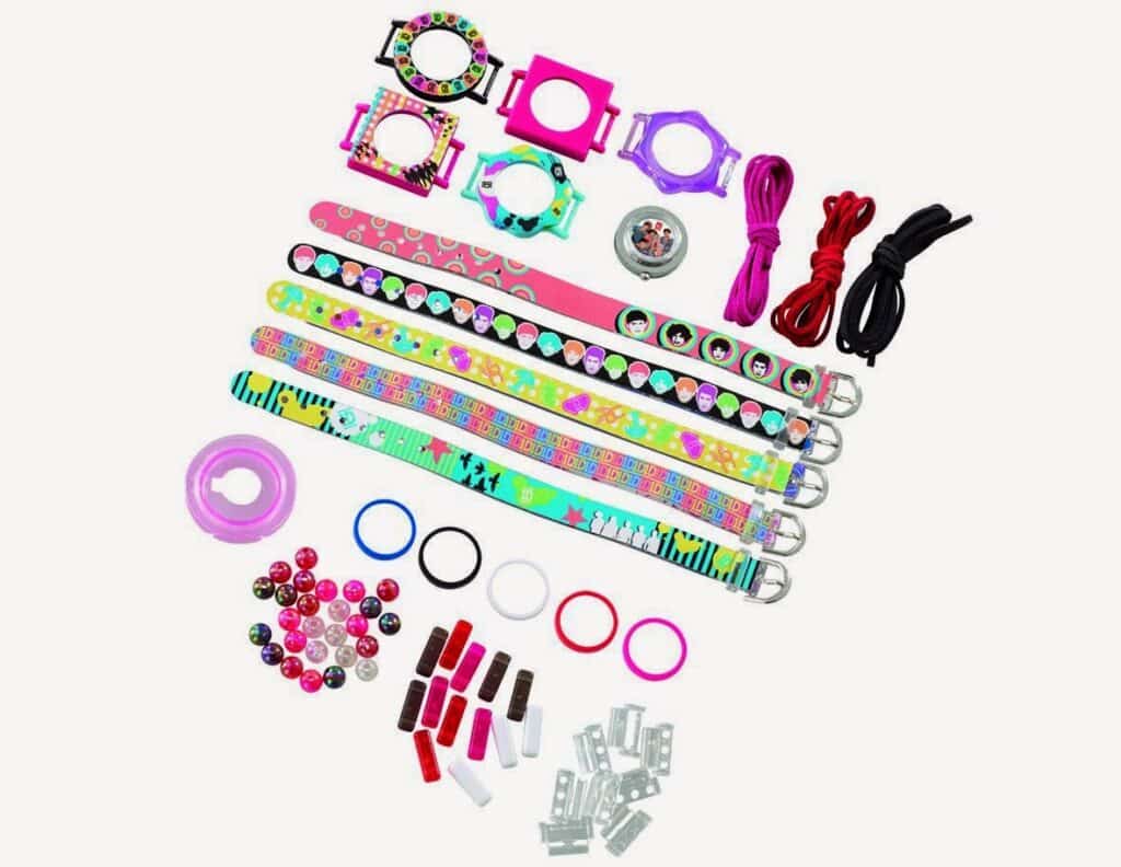 A DIY craft kit with five colourful wristbands, decorative beads, circular frames, cords, small charms, clips, connectors, and rings, all arranged on a white background. The kit features bright, playful patterns and accessories for making custom bracelets.