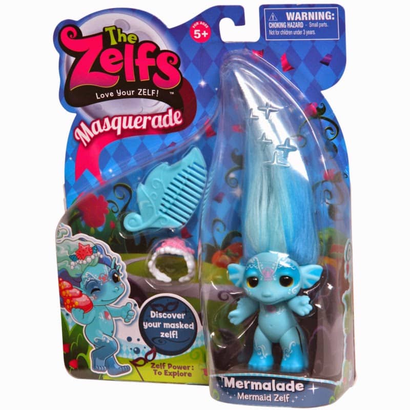A packaged toy called "The Zelfs Masquerade" for ages 5+, featuring a blue Zelf doll named Mermalade with long blue hair, a blue comb, and a ring. The packaging has colourful, aquatic-themed graphics and a small warning label in the top right corner.