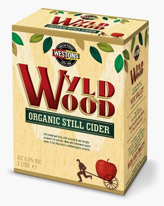 A beige rectangular box of Westons Wyld Wood Organic Still Cider. The label features green leaves, a red apple, and a small illustration of a person pushing an apple in a wheelbarrow. The text highlights it's organic cider with 6.0% alcohol, 3 litres.