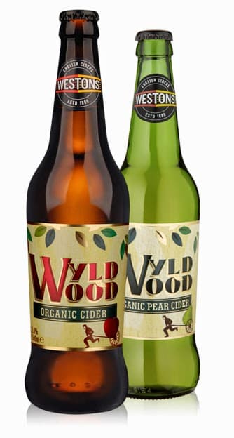 Two bottles of Westons Wyld Wood cider stand side by side. The brown bottle is labelled “Organic Cider” with a red apple graphic, whilst the green bottle is labelled “Organic Pear Cider” with a pear graphic. Both labels feature leaves and a small tree silhouette.