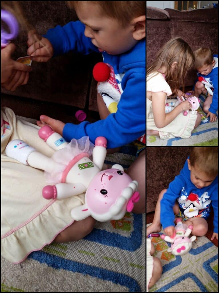 Two young children sit on a colourful rug, playing doctor with a pink lamb doll. The girl holds the doll while the boy applies a pretend bandage. The doll has bandages on its legs. Both kids are focused, sitting close together and playing cooperatively.