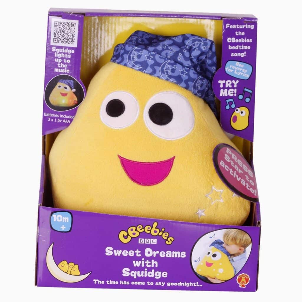 A yellow plush toy named Squidge with a blue nightcap sits in purple CBeebies packaging. Text reads “Sweet Dreams with Squidge.” The toy has big eyes, a smiling mouth, and lights up. An image shows a child pressing Squidge. For ages 10 months and upwards.