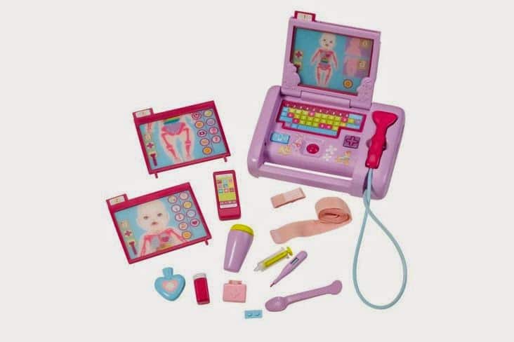 A pink and purple toy doctor’s kit features a laptop with medical images on the screen, charts, a toy phone, syringe, stethoscope, plasters, medicine bottles, a thermometer, tweezers, and a spoon, all arranged on a white background.