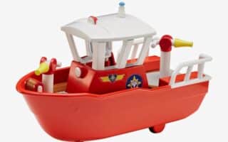 A bright red toy boat with a white cabin, yellow and red details, and stickers resembling badges on the side. The boat has a small deck, a yellow megaphone, and a steering wheel. The design is cartoonish and playful, set against a plain white background.