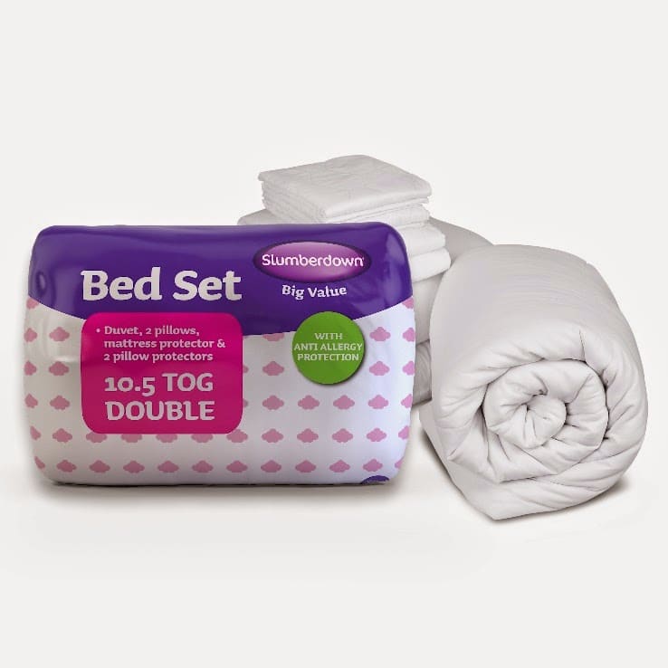 A packaged Slumberdown Bed Set labelled "10.5 TOG DOUBLE" sits next to a rolled-up white duvet and stacked white pillows. The packaging highlights that the set includes pillows, a duvet, a mattress protector, and pillow protectors.