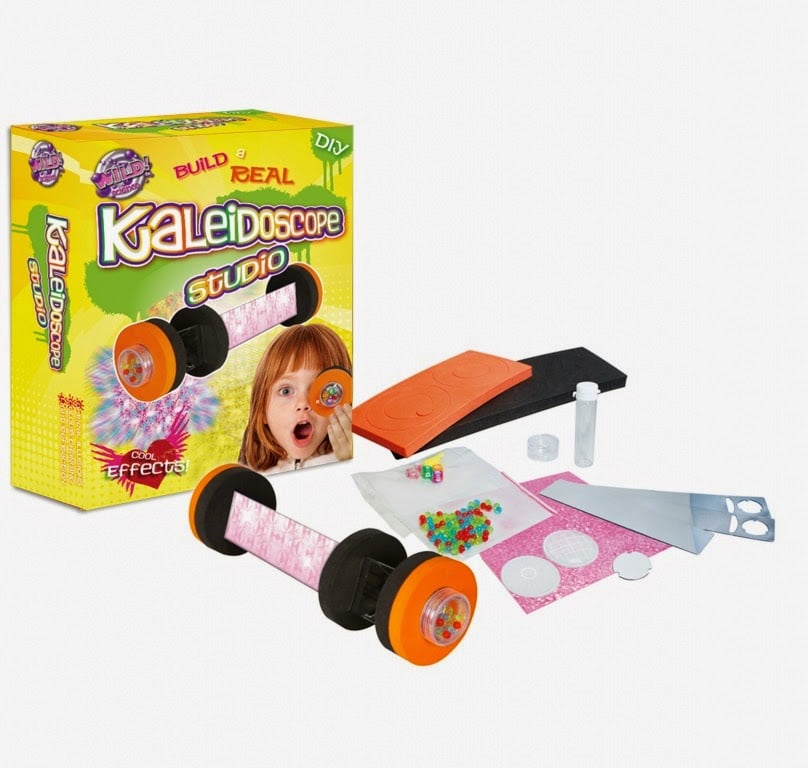 A DIY kaleidoscope kit is displayed. The yellow box reads “Kaleidoscope Studio” and shows a child looking through a kaleidoscope. In front are kit parts: black tube, orange ends, coloured beads, clear discs, stickers, plastic tube, felt, orange tool, and instructions.