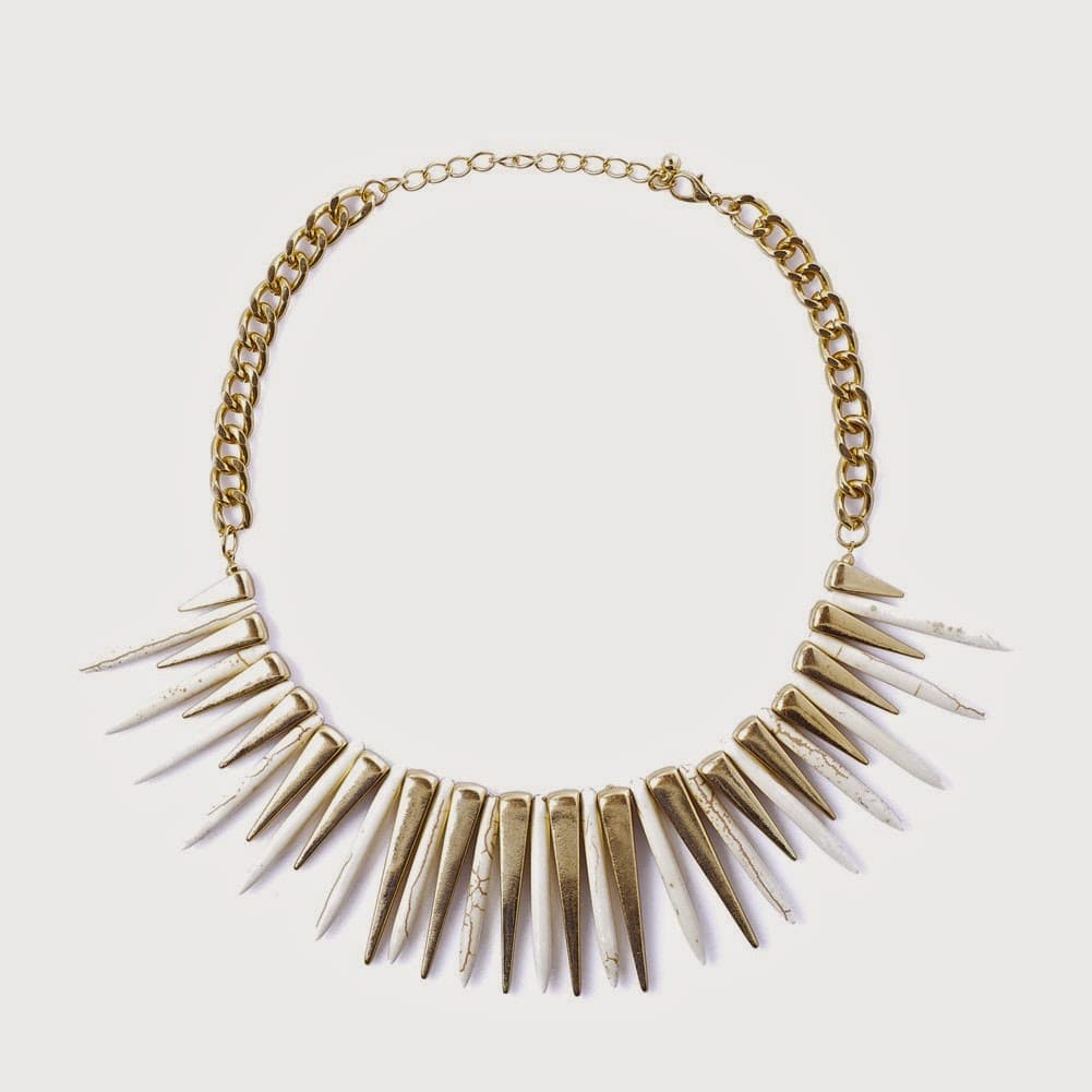 A gold necklace with a chunky chain and an array of long, pointed, spike-shaped pendants arranged in a fan shape, each pendant hanging downwards. The background is plain white.