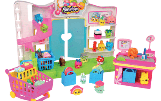 A colourful Shopkins toy supermarket playset with miniature Shopkins characters, shopping trolley, checkout counter, and shelves filled with small grocery-themed figures and accessories arranged around a bright shop backdrop.