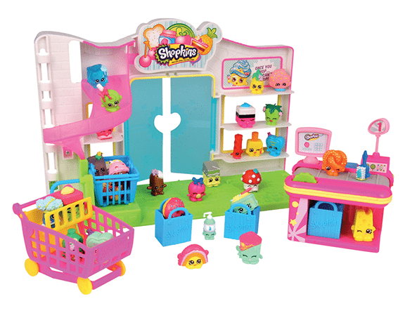 A colourful Shopkins toy supermarket playset with miniature Shopkins characters, shopping trolley, checkout counter, and shelves filled with small grocery-themed figures and accessories arranged around a bright shop backdrop.