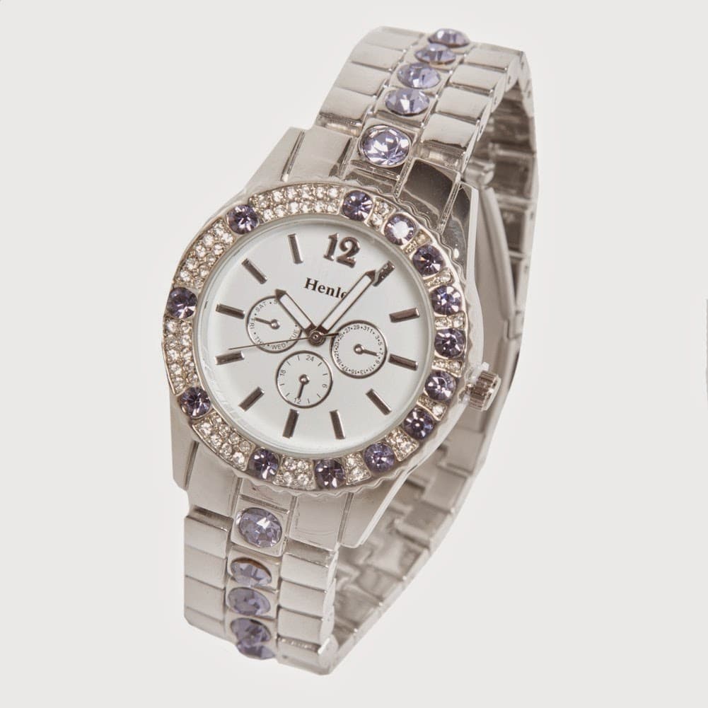 A silver wristwatch with a white face, three small sub-dials, and silver hands. The bezel and metal strap are adorned with alternating clear and purple gemstones. The brand "Henley" is printed below the 12 o'clock marker. The watch is set against a white background.