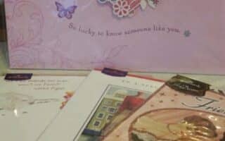 A pink card with a heart and butterflies reads “Friend” and “So lucky to know someone like you.” Several other colourful greeting cards are spread in front of it, some featuring artwork and cursive text.