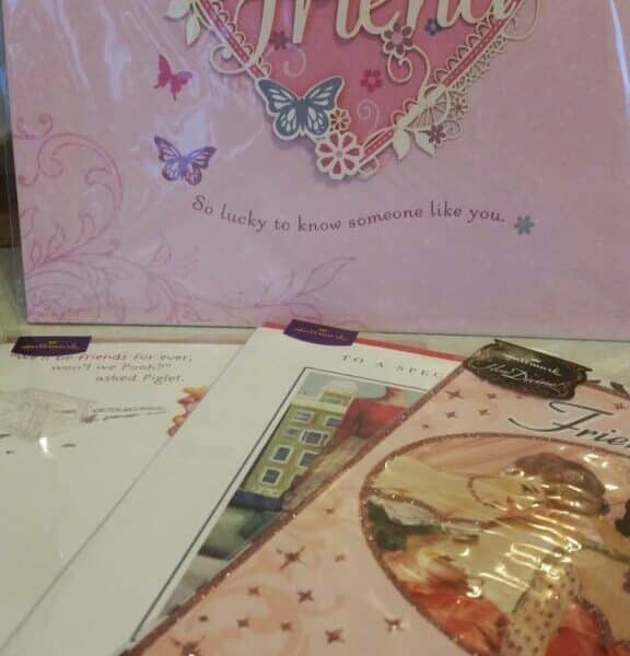 A pink card with a heart and butterflies reads “Friend” and “So lucky to know someone like you.” Several other colourful greeting cards are spread in front of it, some featuring artwork and cursive text.