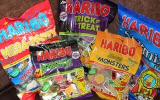 Several colourful bags of HARIBO gummy sweets are displayed on a brown surface. Visible flavours include Mega Party, Trick or Treat, Starmix, HorrorMix, and Terrifying Monsters, each bag featuring playful designs and cartoon gummy bears.