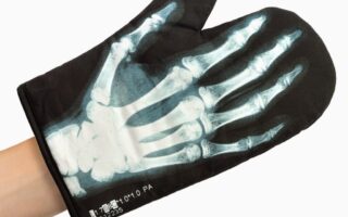 A black oven glove features a printed X-ray image of a human hand, showing white bones and joints in detail. The glove is worn on a left hand, with a small hanging loop visible, and the background is plain white.
