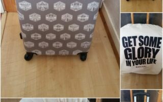 A hard-shell suitcase with travel stamp designs stands on a wooden floor. Close-ups show a fabric cover labelled "Suitcase Glory" and another cover reading "Get Some Glory in Your Life." The suitcase has four wheels and is shown from various angles.