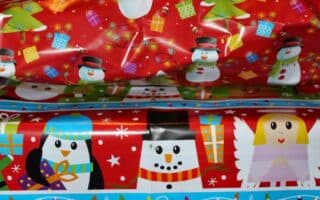 Two wrapped presents stacked on top of each other. The top gift is in red paper with snowmen, Father Christmas faces, gifts, and trees. The bottom gift is wrapped in blue paper decorated with penguins, polar bears, reindeer, angels, and Father Christmases holding presents.
