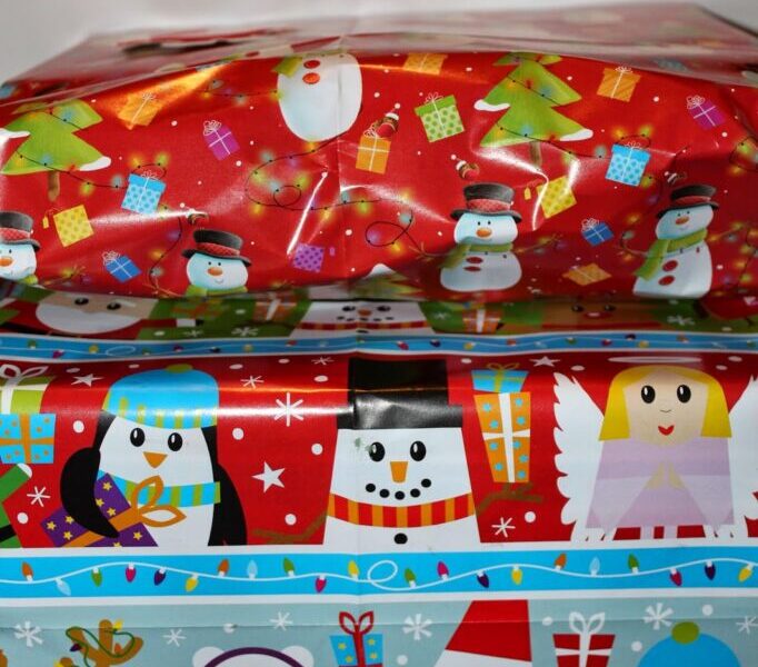 Two wrapped presents stacked on top of each other. The top gift is in red paper with snowmen, Father Christmas faces, gifts, and trees. The bottom gift is wrapped in blue paper decorated with penguins, polar bears, reindeer, angels, and Father Christmases holding presents.