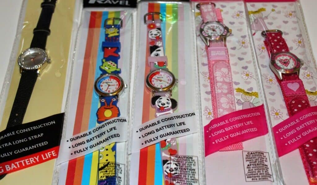 Five packaged wristwatches are displayed side by side. The first has a plain black strap, whilst the others feature colourful designs with animals, pandas, kittens, and unicorns. Each package highlights features like durability and long battery life.