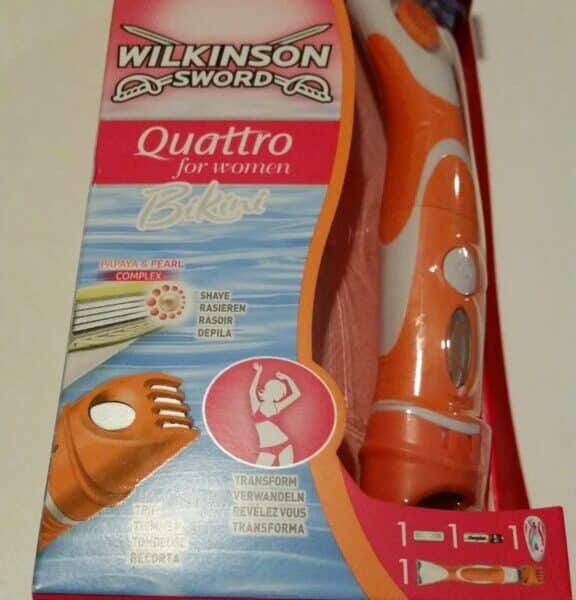A pink and orange box of Wilkinson Sword Quattro for Women Bikini razor. The packaging shows the razor inside, with a trimmer and blade visible. Text highlights its 2-in-1 use for shaving and trimming, with images demonstrating both functions.