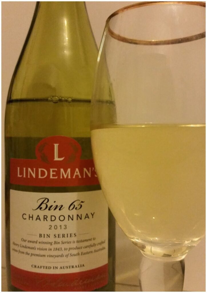 A close-up of a bottle of Lindeman’s Bin 65 Chardonnay 2013 with a partly filled glass of white wine in front. The bottle label is visible, showcasing the brand, wine type, vintage year, and origin—crafted in Australia.
