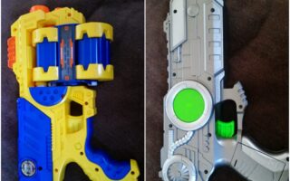 The image shows two colourful toy guns on a dark surface. The left toy is blue, yellow, and orange with a bulky, cylindrical chamber. The right toy is silver and grey with green accents, a sci-fi design, and a bright green trigger.