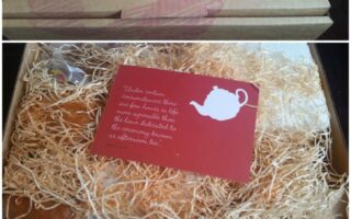 A collage shows a delfinann.co.uk gift box with pink branding, filled with straw. Inside are scones, cakes, a red teapot card, clotted cream, and jam, all arranged neatly. The open box reveals a handwritten note and different treats wrapped separately.