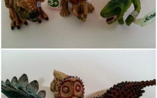 Two rows of toy dinosaur figurines on a white surface. The top row includes brown and green dinosaurs with Schleich tags on their legs. The bottom row shows a blue Stegosaurus, a brown Triceratops skull, and two more dinosaurs with similar tags.
